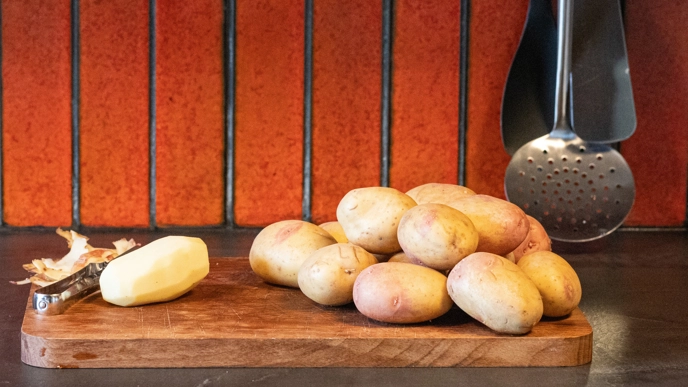 Potatoes on a cutting board. One is peeled.