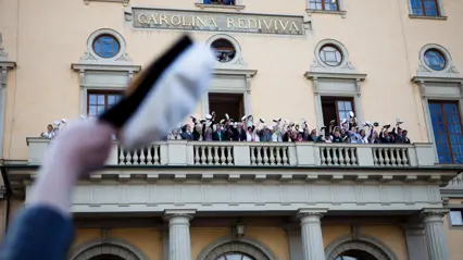 Someone is waving a graduation cap and in the background, there is an impressive building.
