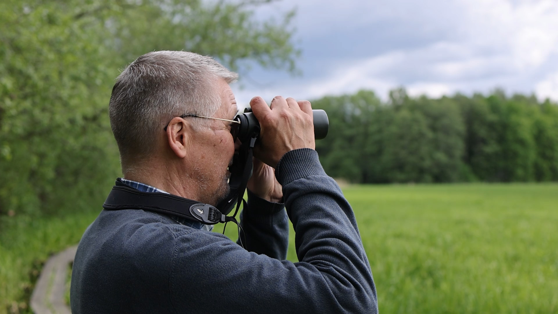 Man i naturmiljö tittar i kikare. Foto