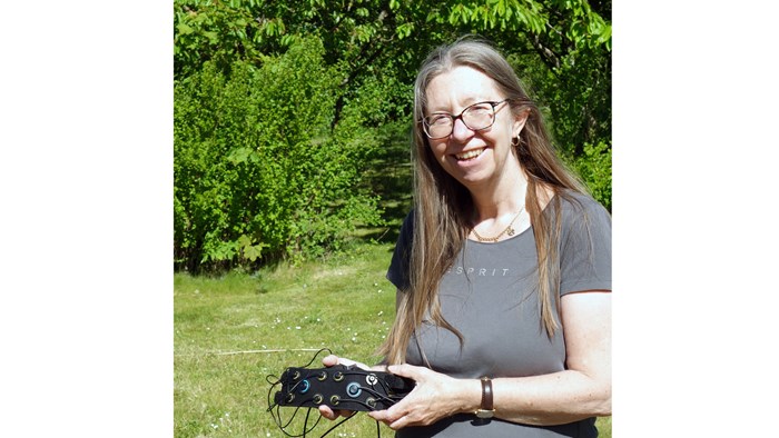 A smiling woman holding a belt with electrodes. Photo.