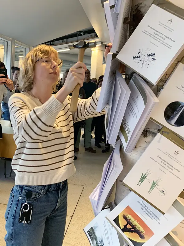 Woman nailing a book to a tree.