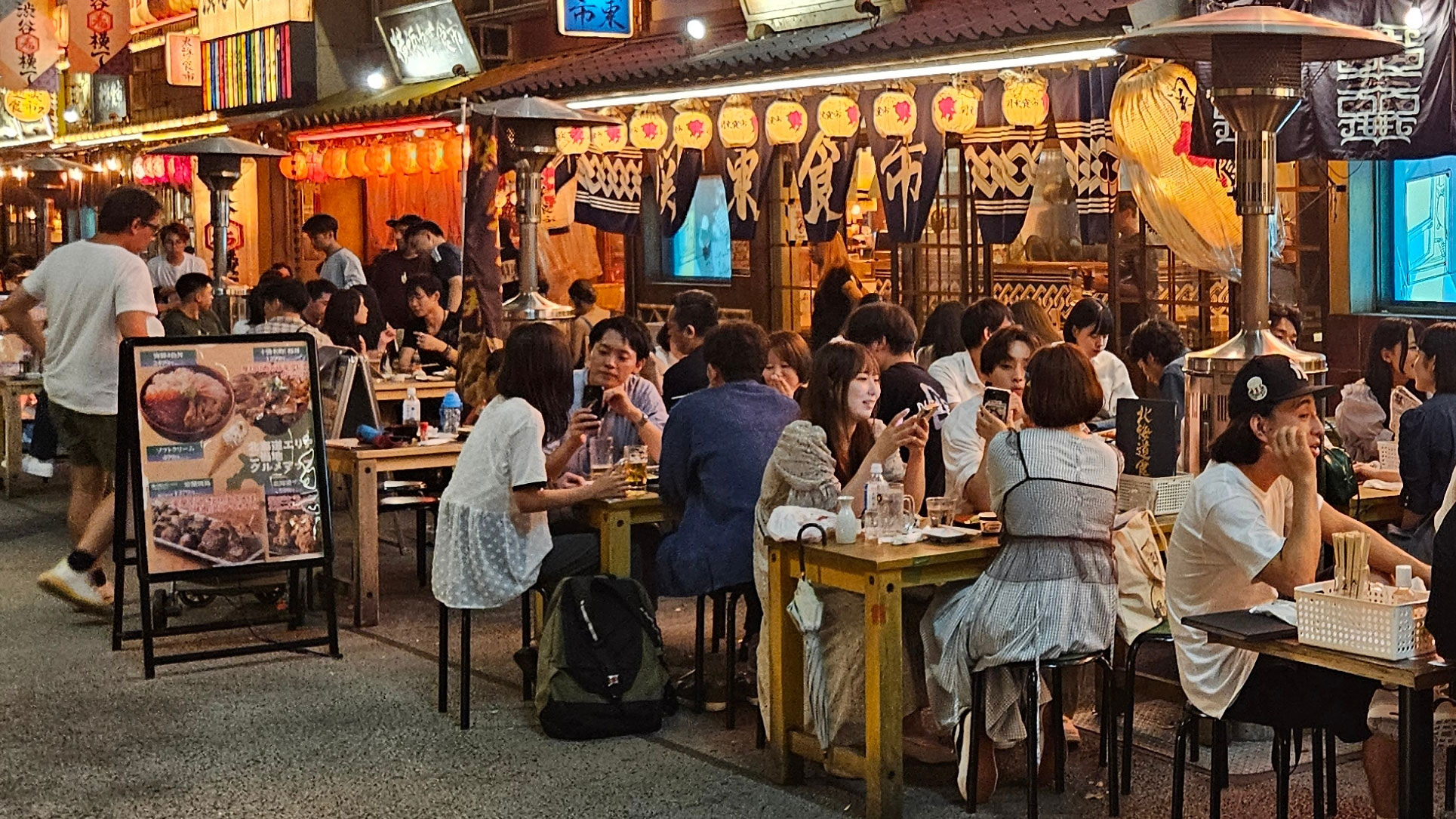Tokyo, Japan: Locals and tourists dine under glowing lanterns at a lively izakaya street filled with traditional food stalls and outdoor seating.