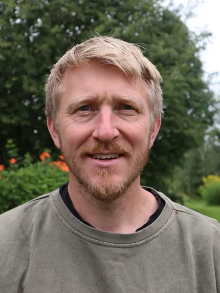 Porträttbild på Albin Gräns utomhus i en park med grönska i bakgrunden.