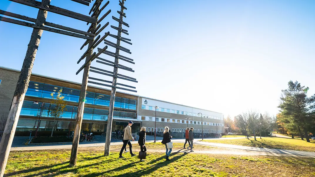 Kontorsbyggnad i bakggrunden med studenter som passerar i förgrunden. Foto.
