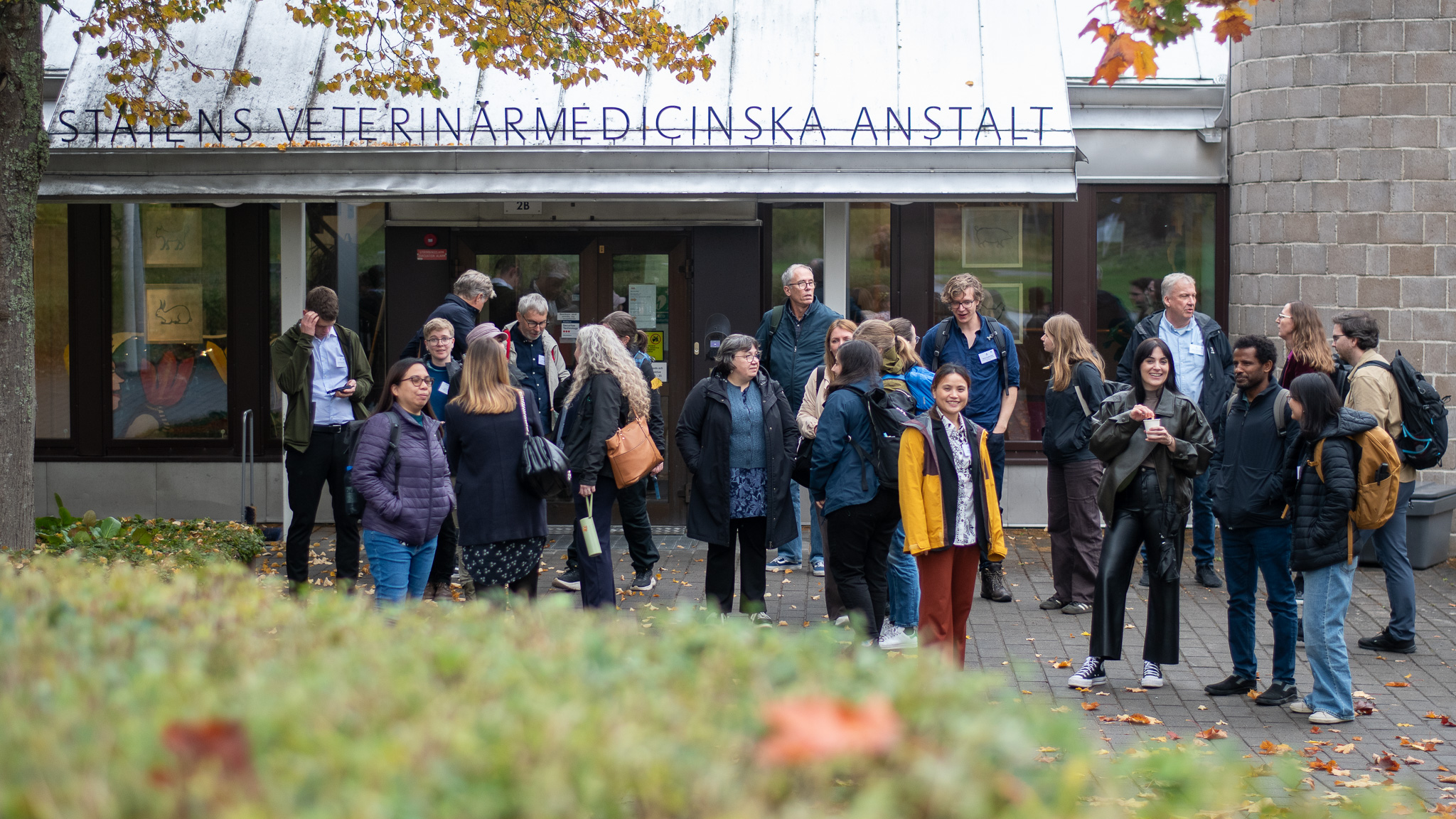 En stor grupp människor står framför en stenbyggnad. Foto.