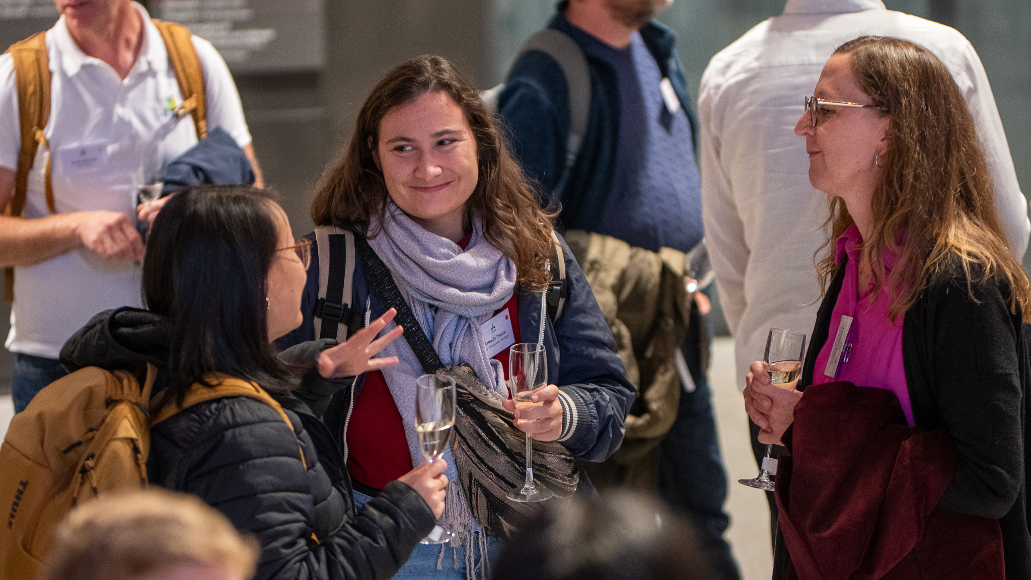 Tre kvinnor med champagneglas i händerna pratar med varandra. Foto.