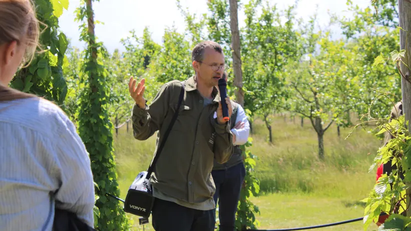Erik de Vahl står bland humlestörar och håller en visning. Han har en bärbar högtalare över axeln.