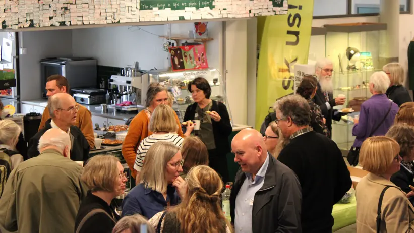 En stor grupp människor minglar med kaffekoppar i handen.