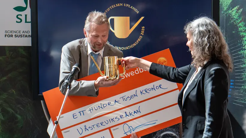 En man tar emot en vattenkanna i guld av en kvinna på en scen. Foto.
