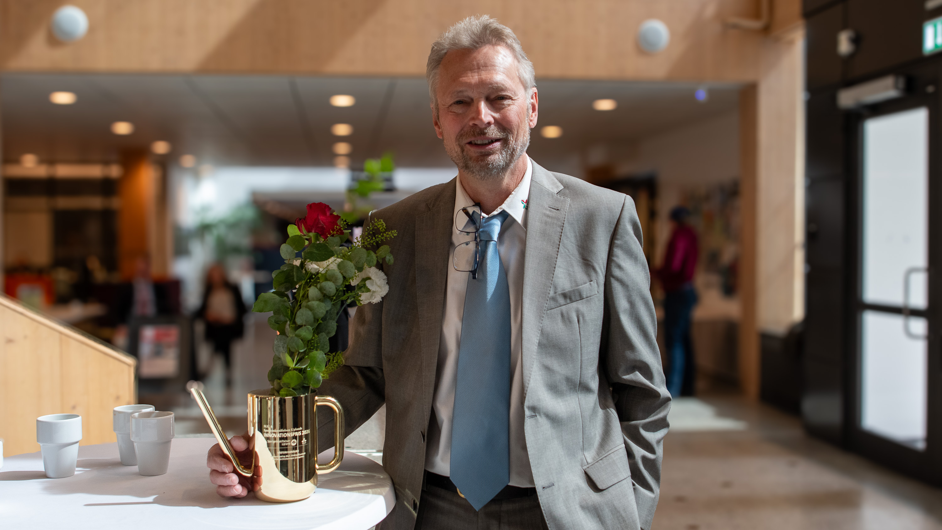 En man inomhus brevid en vattenkanna i guld med blommor. Foto.