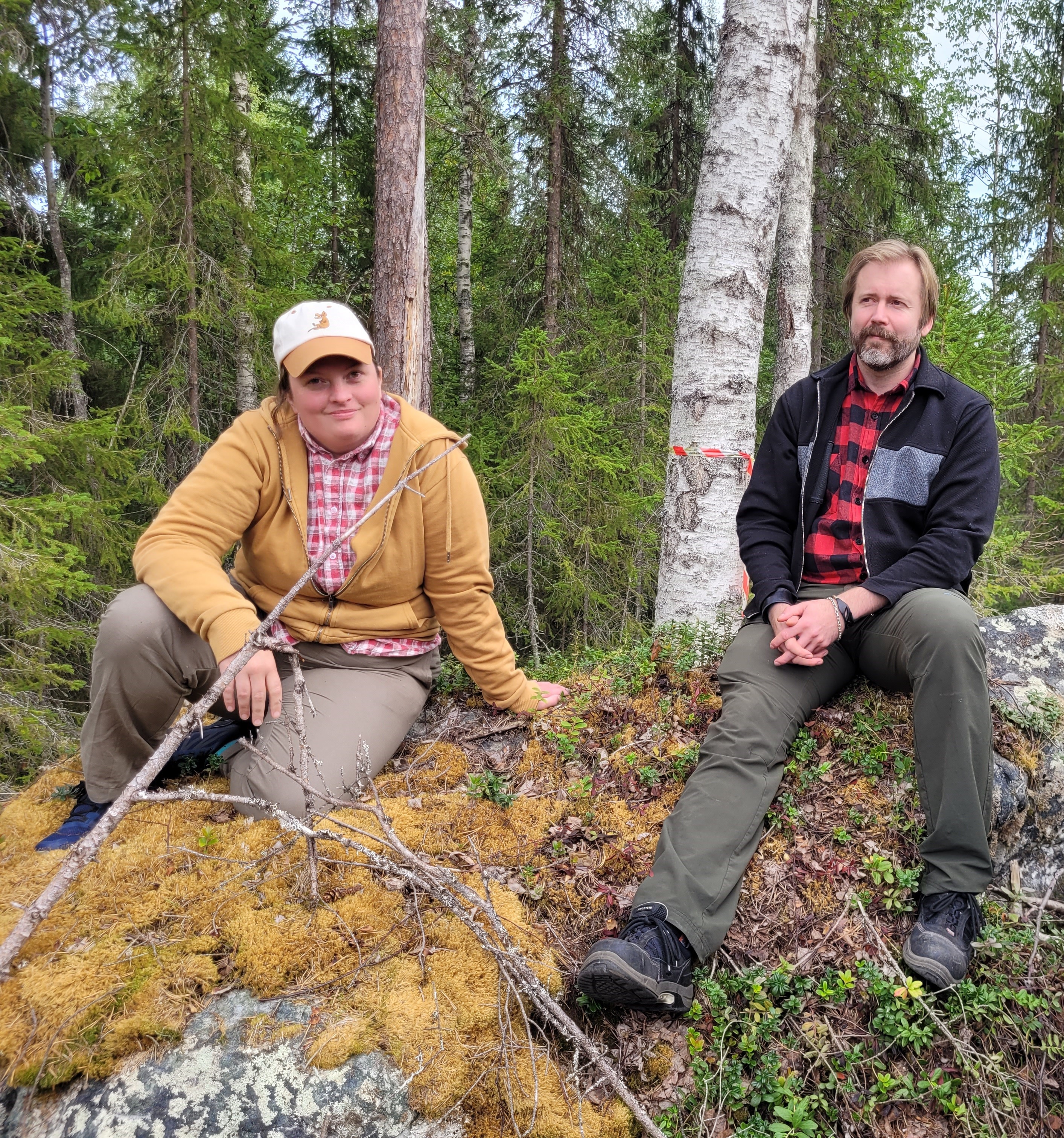 Doktoranderna Sarah och Mathias sitter på en sten i skogen en sommardag. 