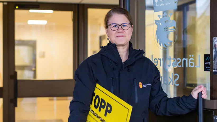 En kvinna står i en dörröppning och tittar mot kameran.