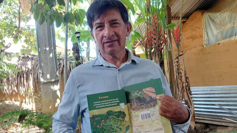A man holds up the newly printed book infron of himself.