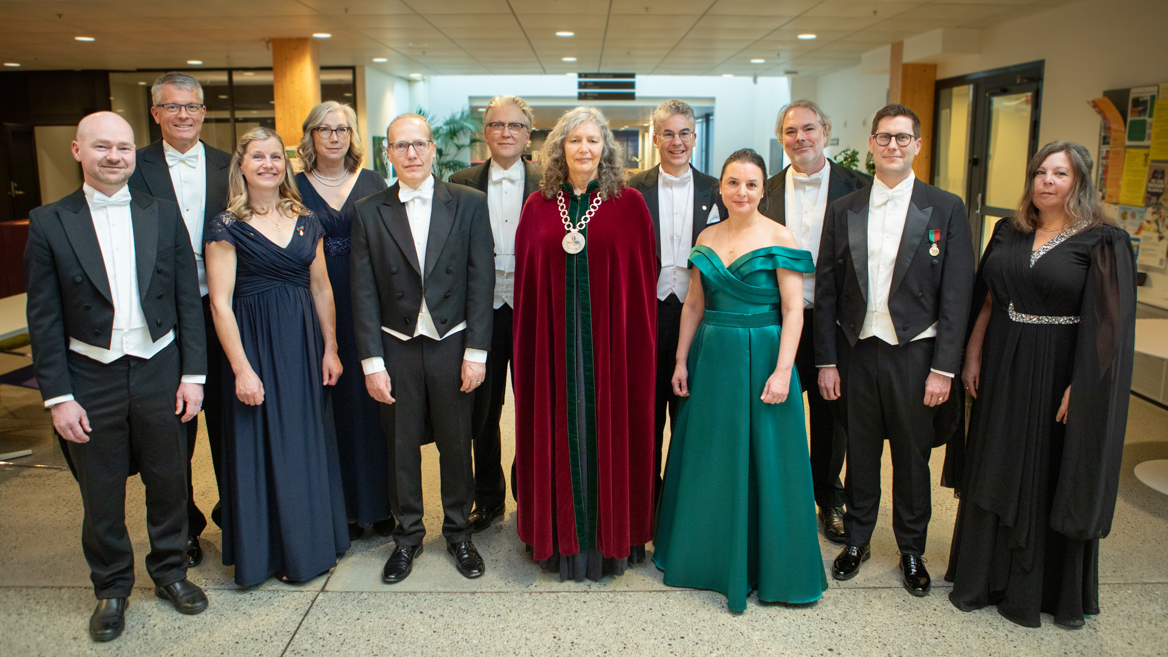 En grupp högtidsklädda personer, i mitten en kvinna med en rektorskedja och en röd sammetskåpa. 