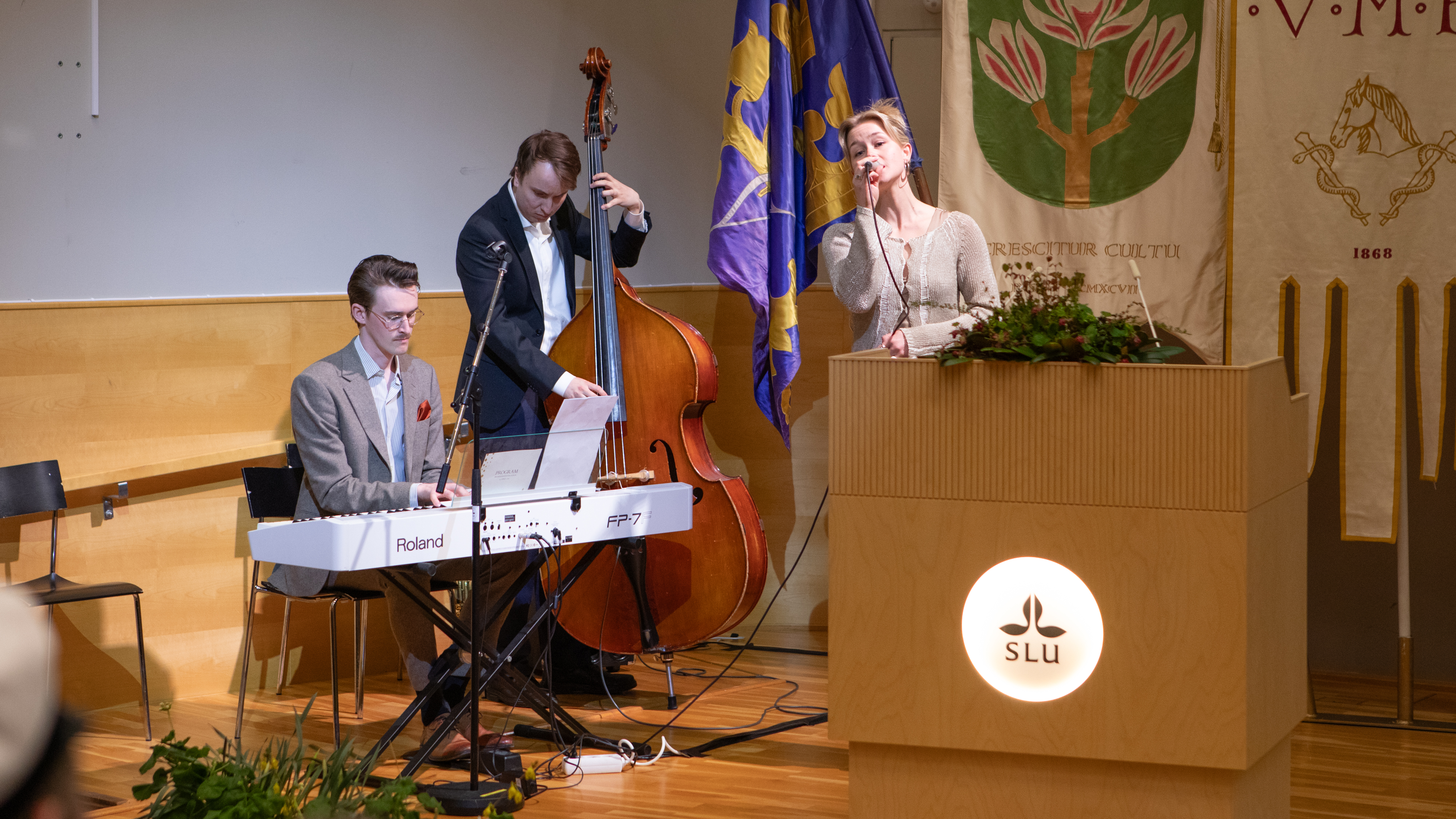 En pianist, en basist och en sångerska framträder på en scen.