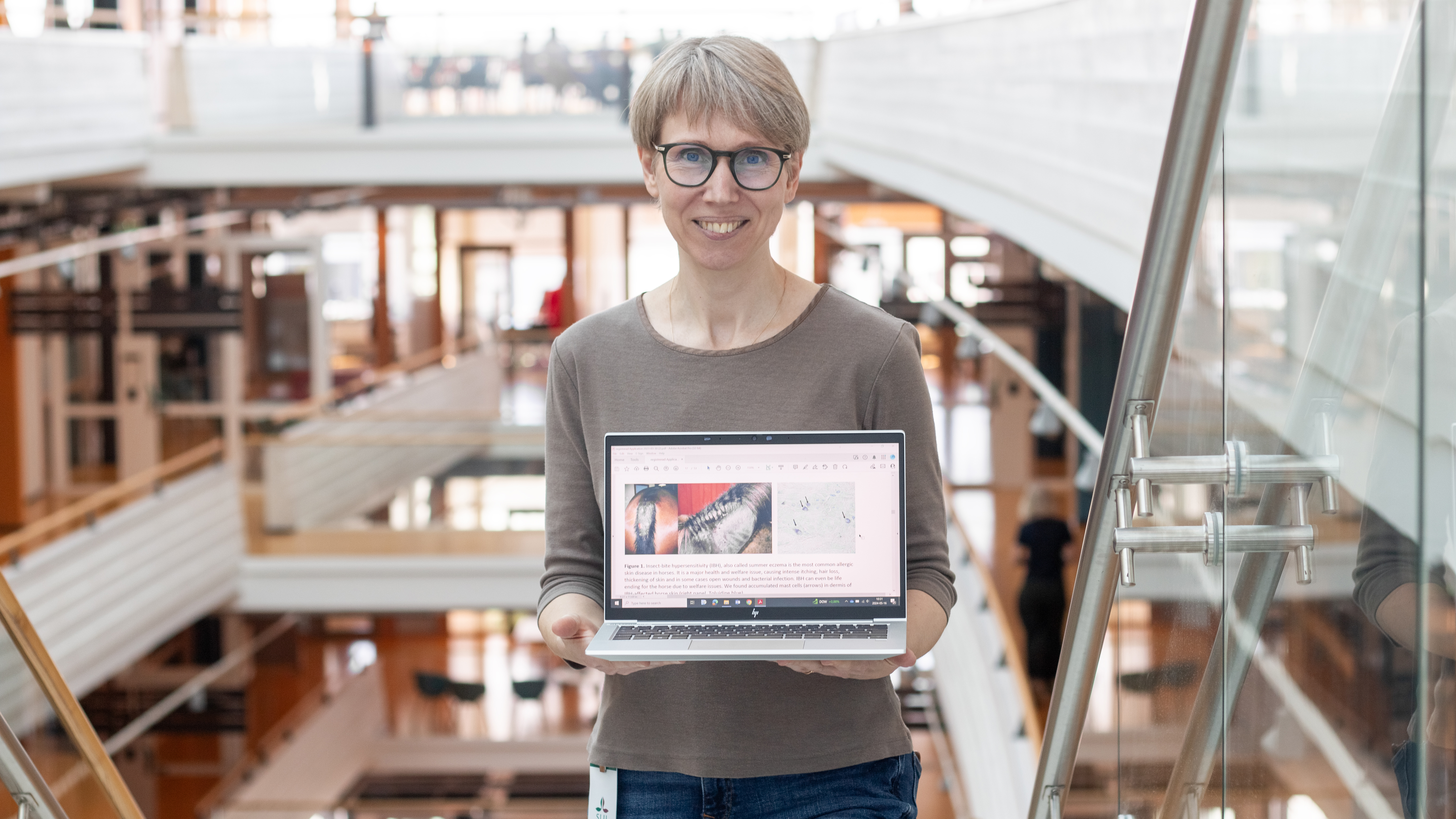 Porträttbild av en kvinna (Sara Wernersson, SLU) som visar upp bilder på hästar med eksem, ståendes inomhus.