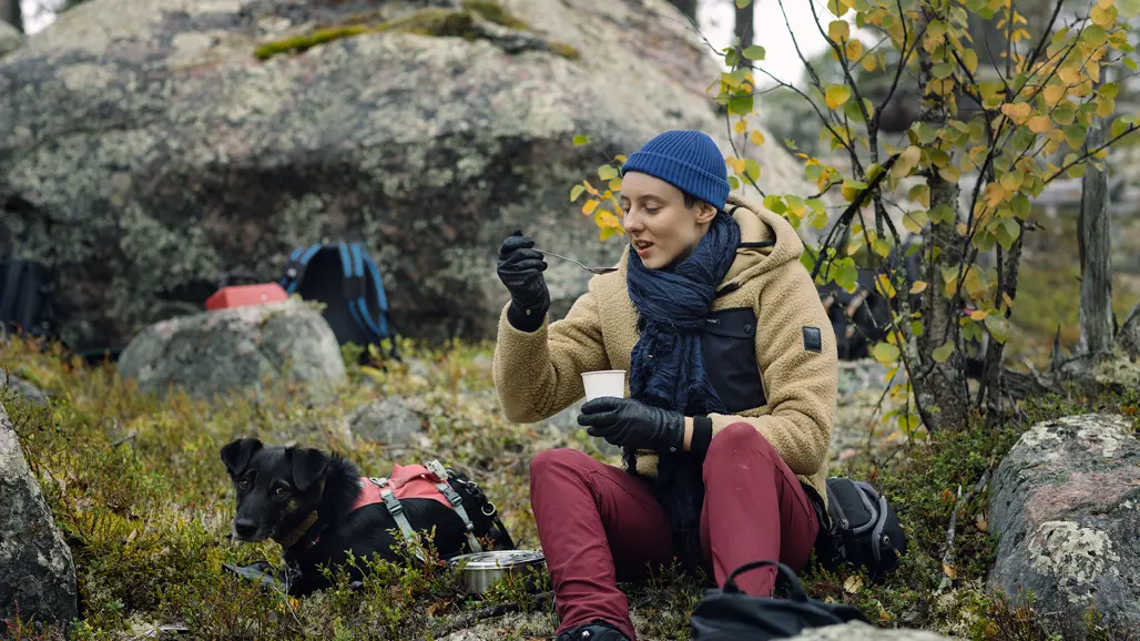 En person som sitter i mossa framför ett stenblock och äter med sked ur en kopp. Foto: Malin Grönborg