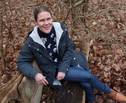 kvinna i blå jacka sitter på en bänk i skogen