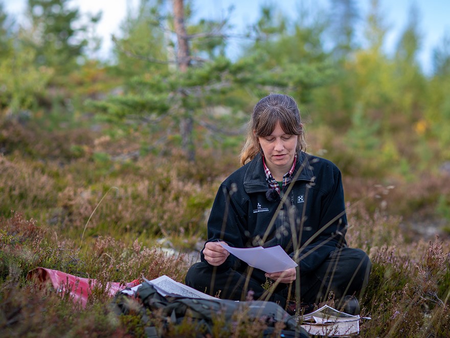 Hilda Mikaelsson, fältchef Riksskogstaxeringen sitter i skogsbacke med fältutrustning framför sig. Foto.