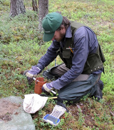 En man tar jordprover i skogsmark, foto.