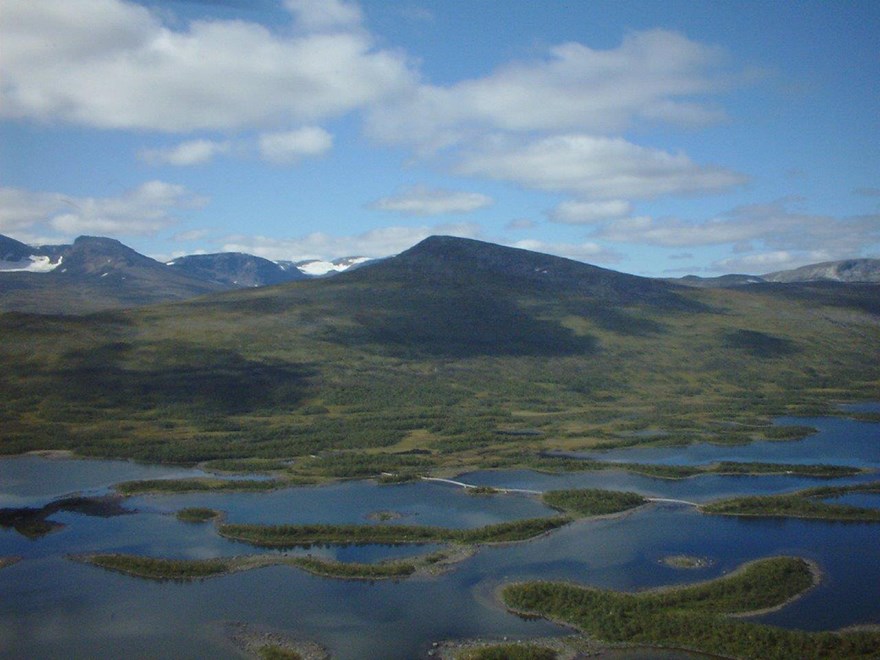 Fjällandskap med vatten i förgrunden. Foto.