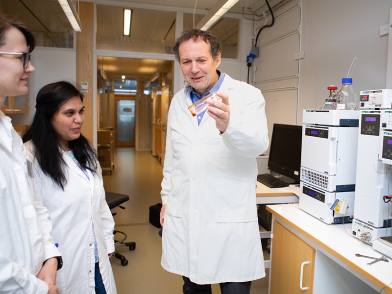 Bild av Volkmar Passoth som pratar med kollegorna Johanna Blomqvist och Yashaswini Nagavara Nagaraj i labbet. Volkmar håller i ett provrör med en röd vätska.  