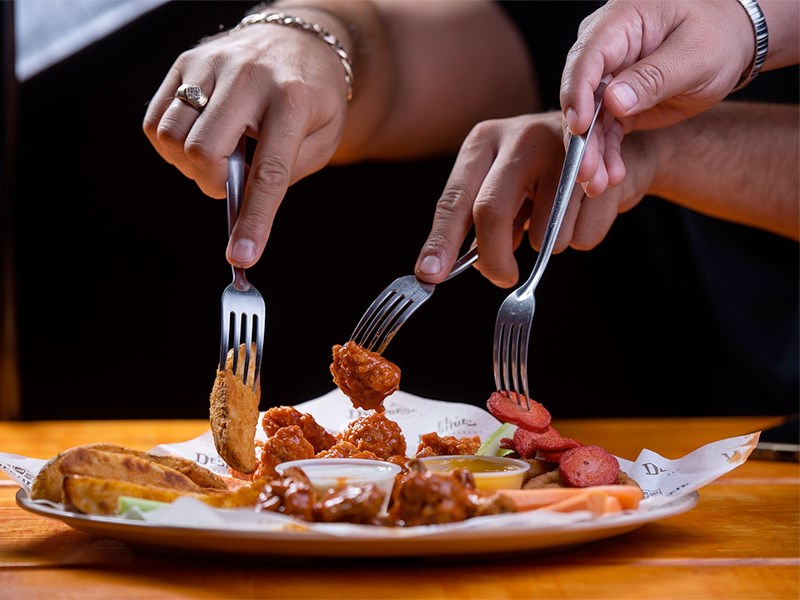 Three hands with forks pick up chicken wings from a plate. Photo. 