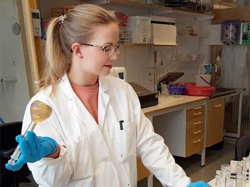 En kvinna håller i en flaska i ett laboratorium. Foto.