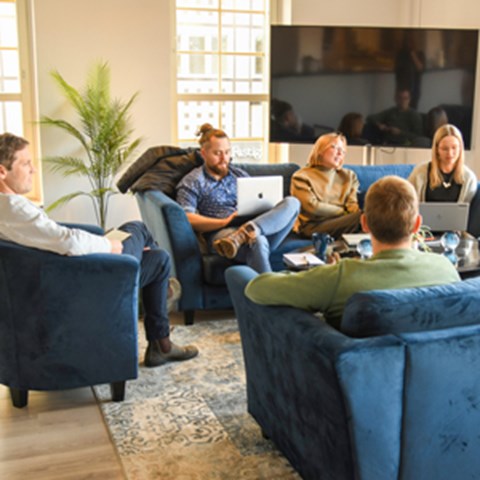 Five people sit on blue sofas and discuss. Photo.
