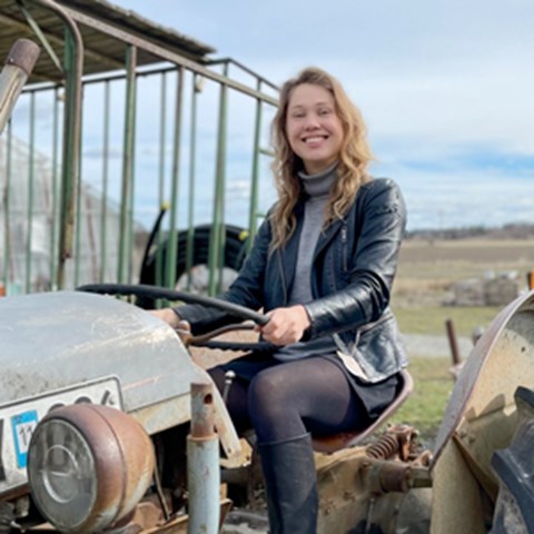 En leende kvinna sitter på en gammaldags traktor. Foto.