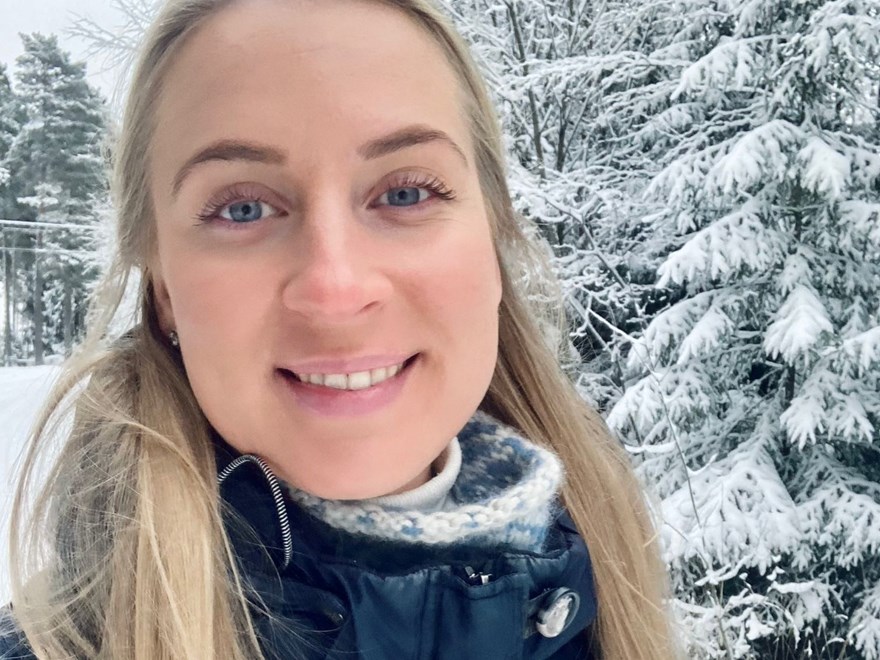 An image of a woman who's smiling at the camera. Outdoors, snow on the ground.