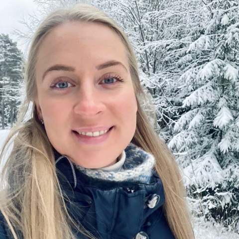 An image of a woman who's smiling at the camera. Outdoors, snow on the ground.
