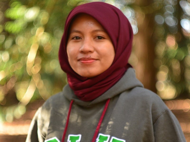 An image of a woman wearing a sweater with the text "SLU". Outdoors.