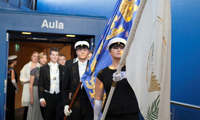 Studenter med flaggor och doktor marscherar. Foto