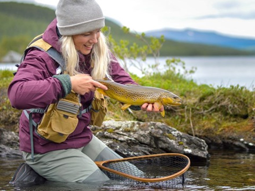 Tjej sitter i vattenbryn och håller i en fisk. Foto.