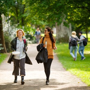 Två kvinnliga studenter promenerar i solig parkmiljö. Foto.