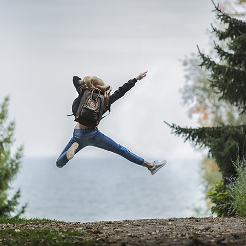 Glad tjej som hoppar i luften, skog på båda sidor. Foto.