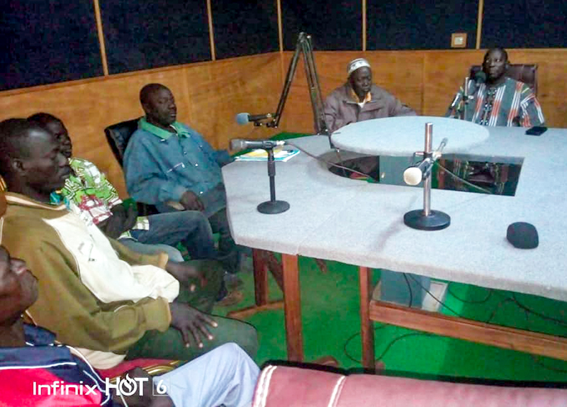 Six people are sitting around a table with microphones in front of them indoors, photo.
