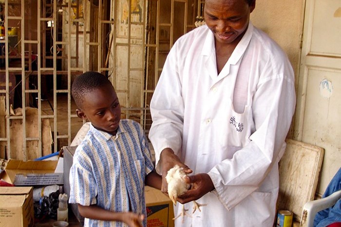 A man and a child is holding a chicken outdoors, photo.