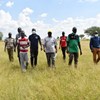 8-10 people comes walking towards the camera in a grassland in Uganda