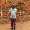 African man stands in front of a mud wall