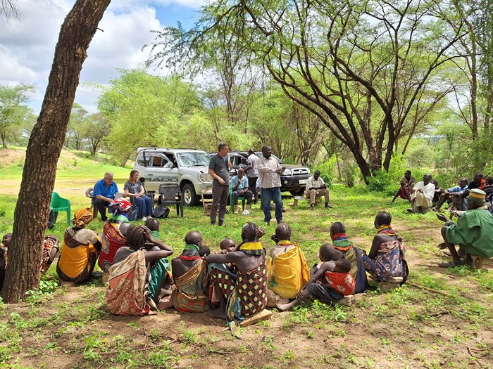 Two persons are talking in front of a group under a tree