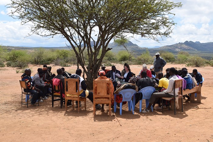 Researcher sitting outside, talking with group of people.