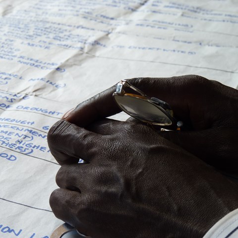 Dark brown hands holding a pair of glasses next to a paper.