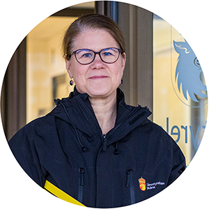 En kvinna står i en dörröppning och tittar mot kameran.