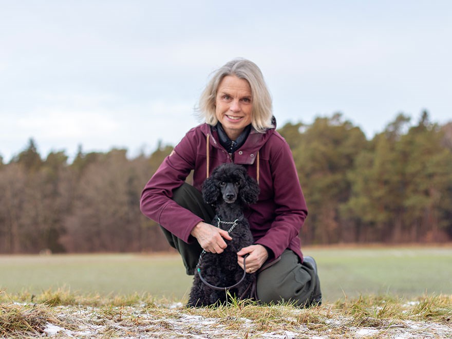 En kvinna sitter på huk intill sin hund.