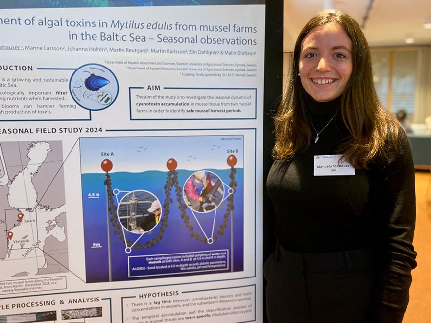 A young woman with long dark hair, standing next to a scientific poster. Photo.