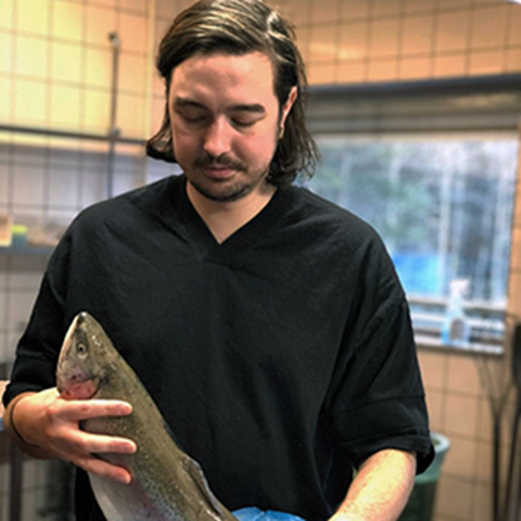 En ung man som står vid ett bord och håller i en fisk. Foto.