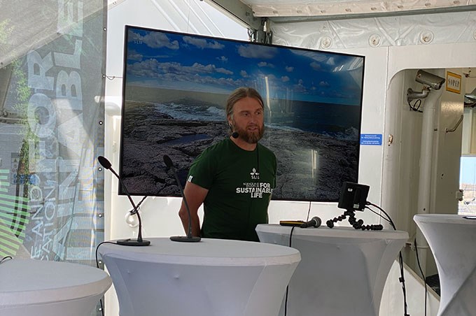 Manlig SLU-forskare med grön SLU T-shirt som står på en scen och håller ett föredrag . I bakgrunden syns en stor skärm som visar powerpointbilder. Foto.