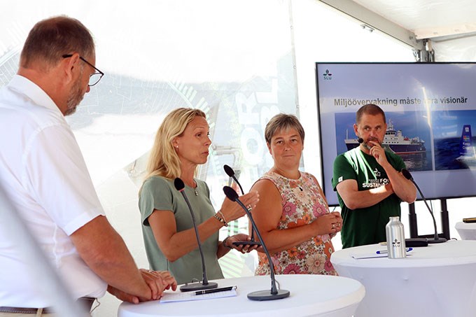 Fyra personer står på en scen och diskuterar under ett seminarium. Foto.